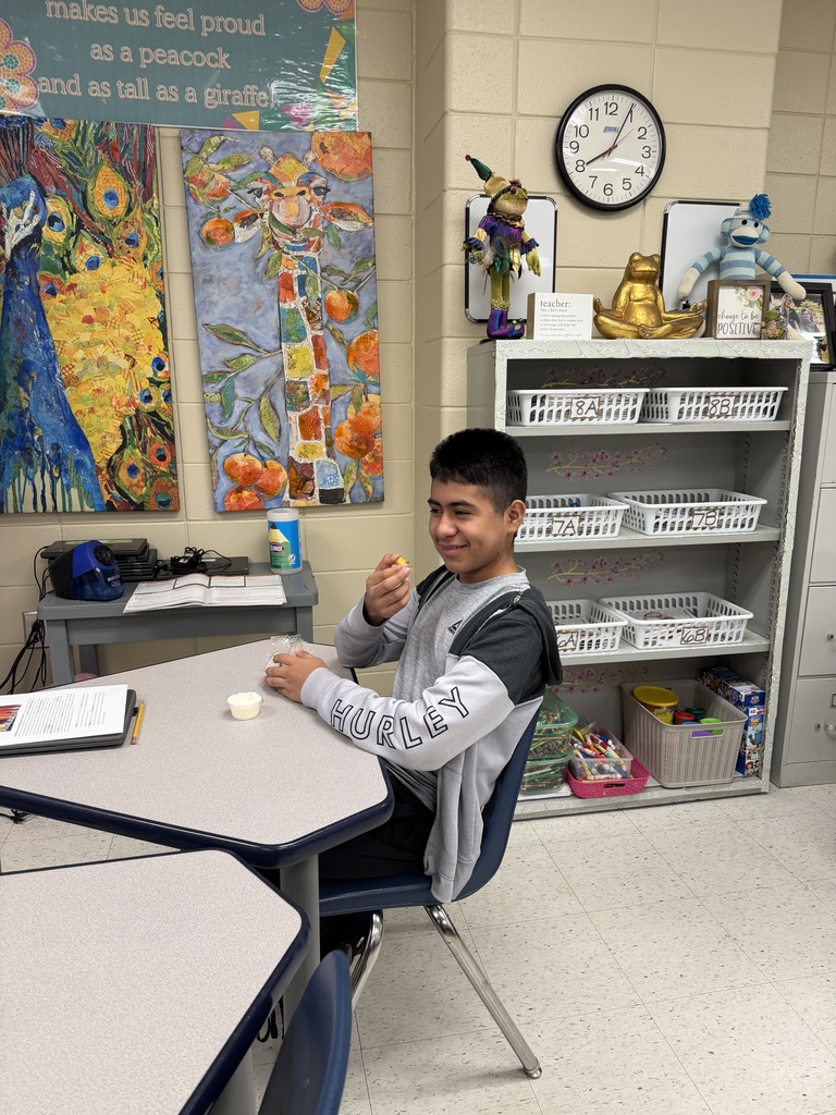 A person sitting at a table eating a snack. A clock and several paintings are on the wall.