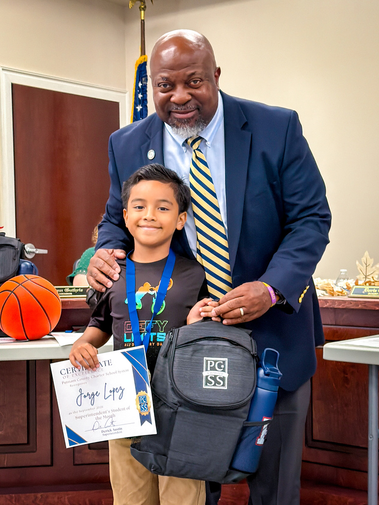 A young boy with a certificate stands beside a man in a suit and tie, smiling.