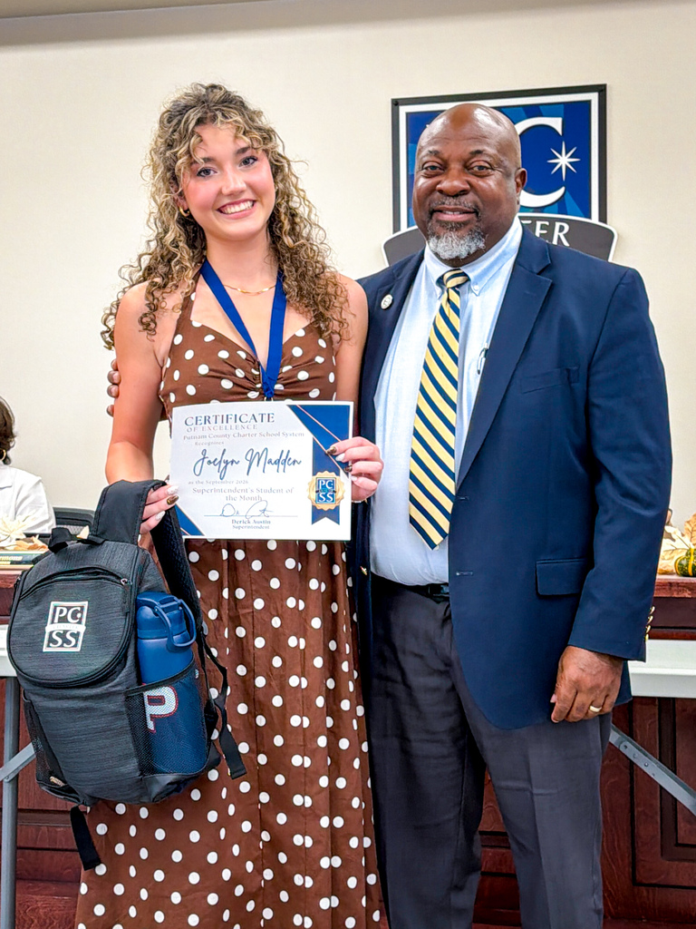 A woman in a polka-dot dress poses with a certificate, while a man in a suit stands next to her.