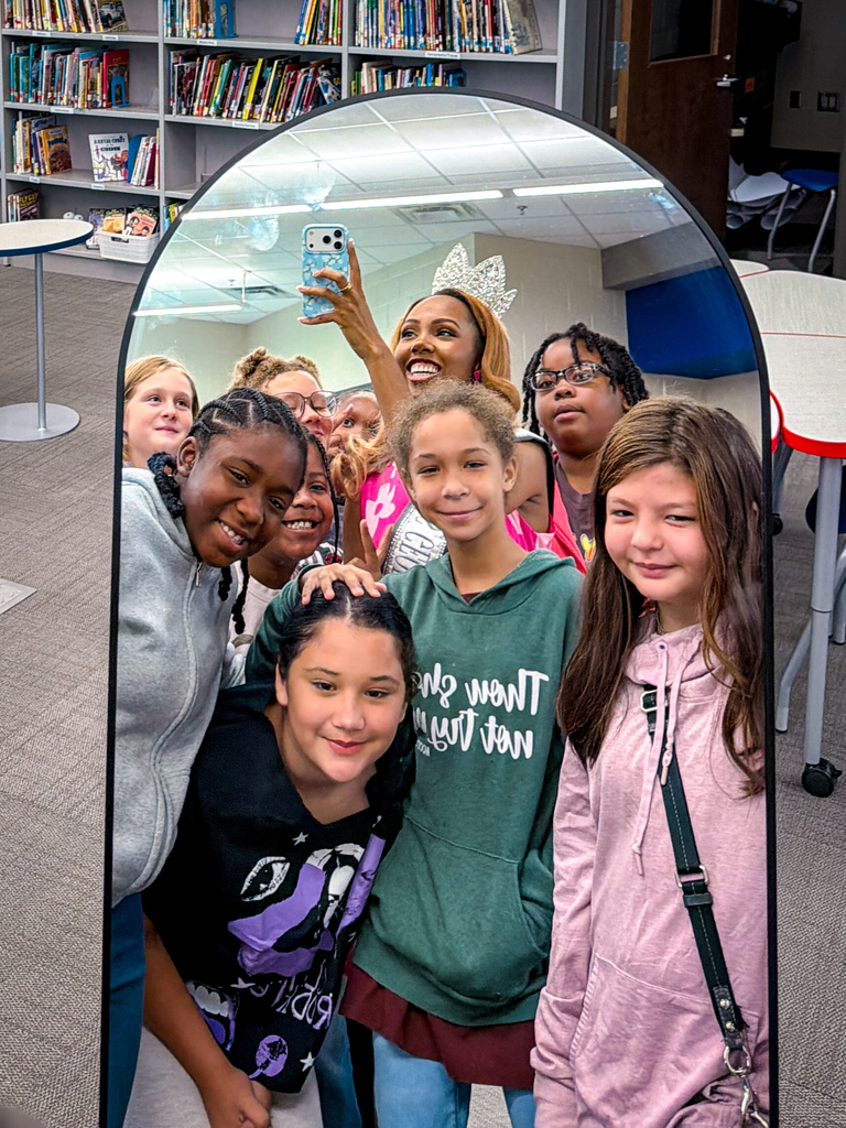 A group of young girls smile for a selfie in front of a mirror in a room.