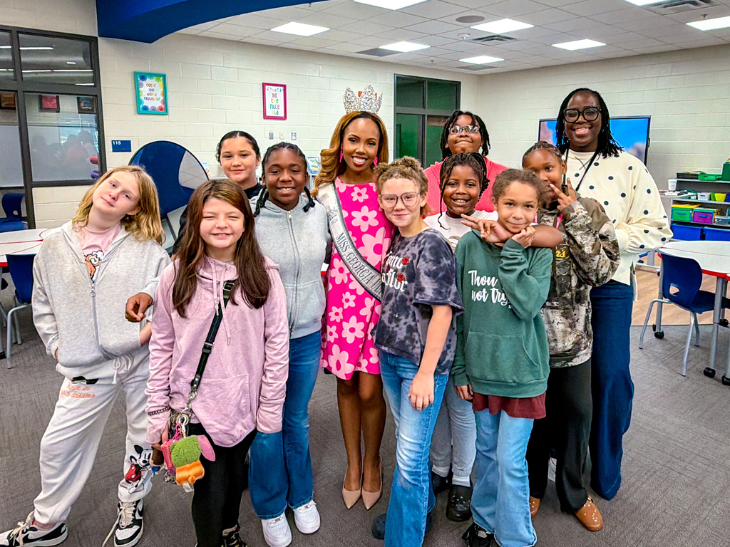 Group of young girls and adults pose for a photo in a classroom with tables and chairs.