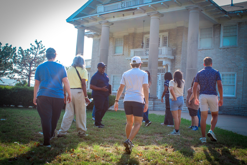 A group of people walks on a lawn in front of a historic building with tall columns.