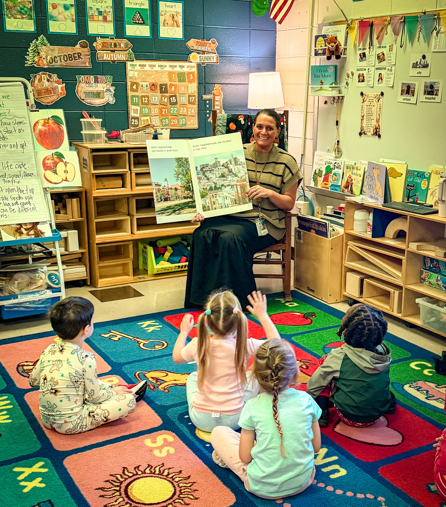 A teacher reads a book to young children sitting on a rug in a classroom.