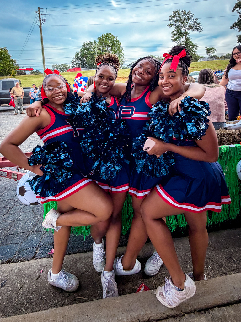 Four cheerleaders in matching blue uniforms pose for a photo at an outdoor event.