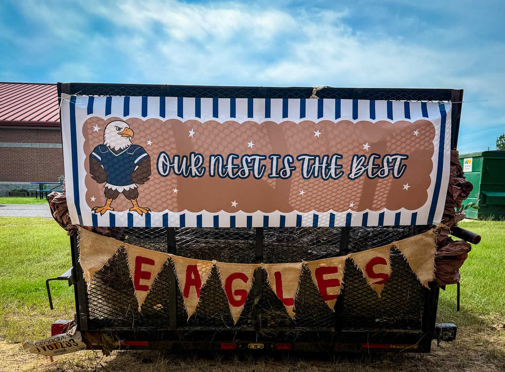 Display on a trailer, a banner with blue, white, and brown stripes. An eagle and "Our nest is the best" are on it.