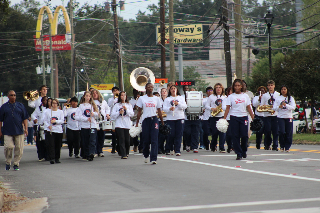 A marching band in white shirts, blue pants, and white hats playing instruments in a parade.
