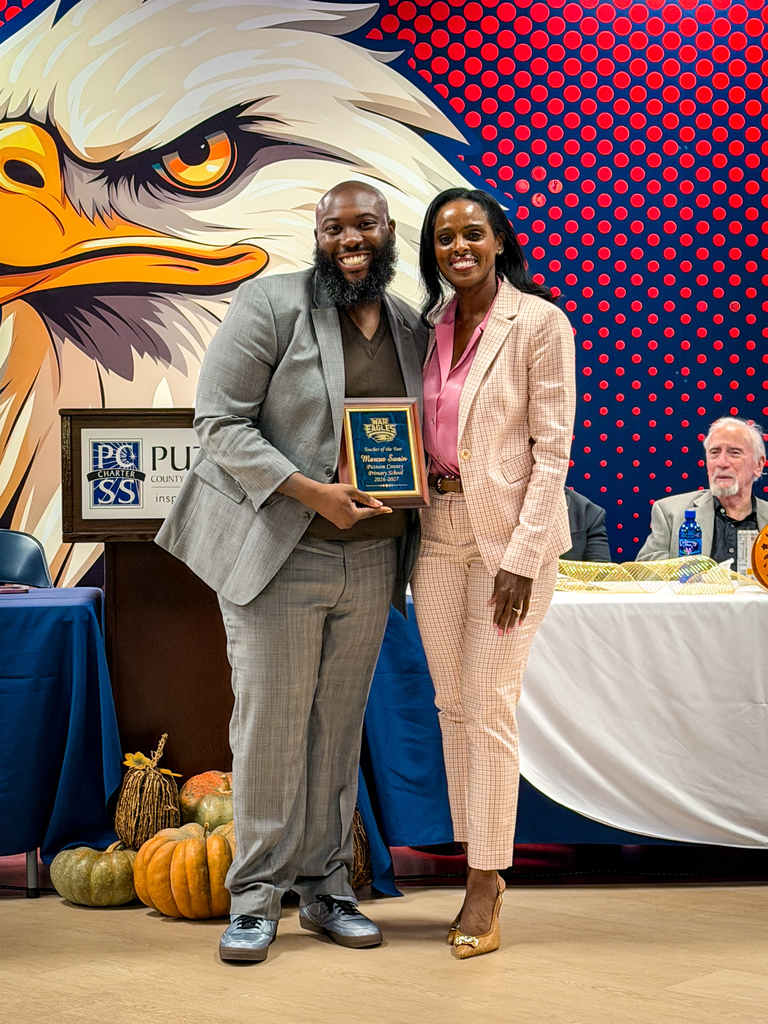 Man and woman stand next to each other holding a plaque, a large eagle mural behind them.