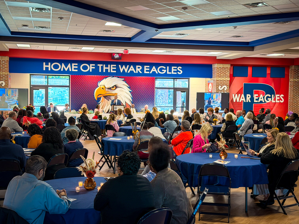Many people seated at tables in a room, some with candles. A banner with an eagle and text.