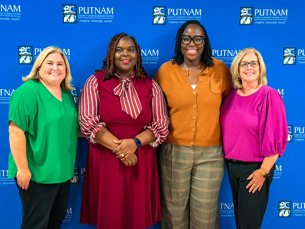 Five women standing together in front of a blue backdrop with Putnam College logos.