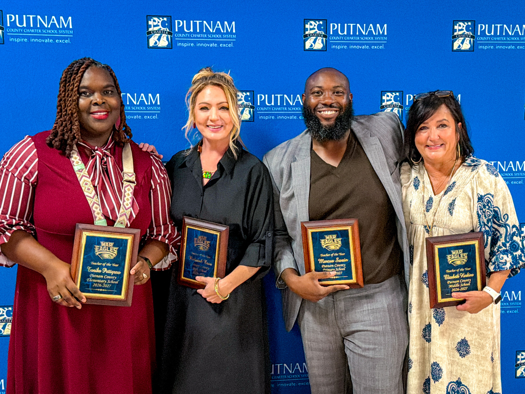 Five adults stand against a blue backdrop, holding framed awards. They smile for the camera.