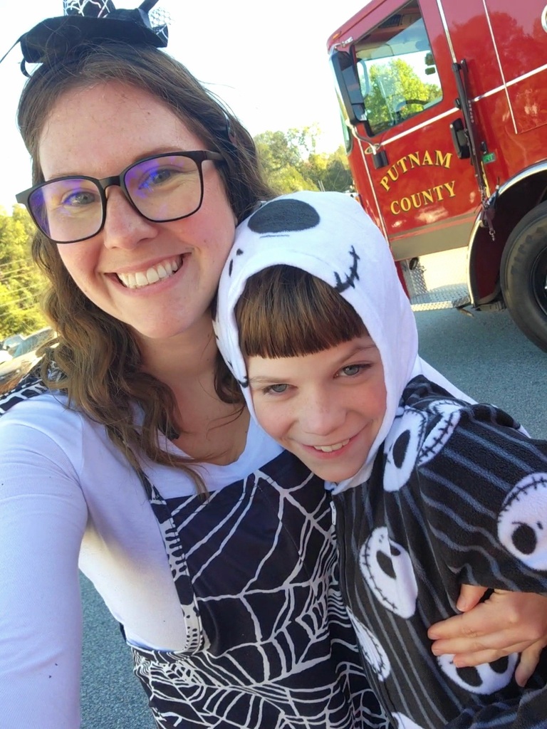 Woman in glasses and a child in a black and white skull shirt stand close, smiling.