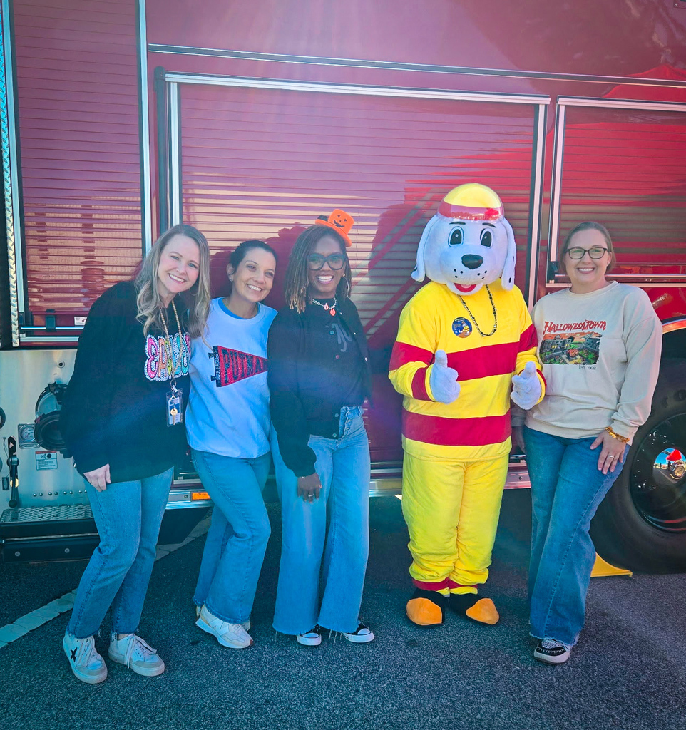 Five people pose for a photo in front of a fire truck; a person in a fire safety mascot costume.