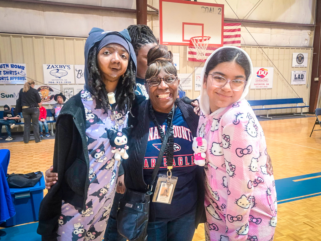 Three people in colorful outfits pose for a photo in a gymnasium with a basketball court.