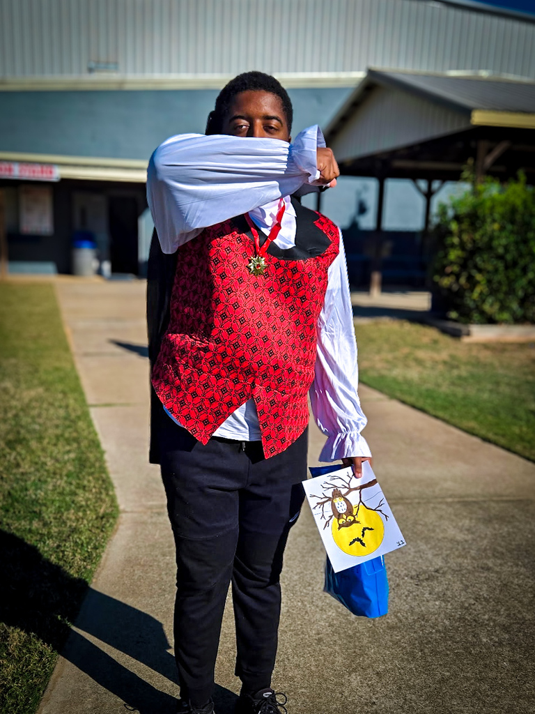 Person wearing red vest with white long sleeves, black pants, and holding a bag with bat design.