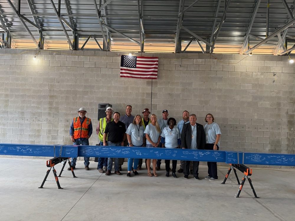Picture of 11 adults standing in front of a blue beam where students signed their names under an American Flag