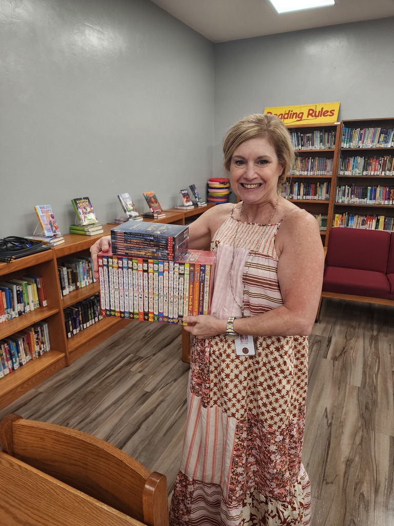 Picture of female teacher holding books in a library.