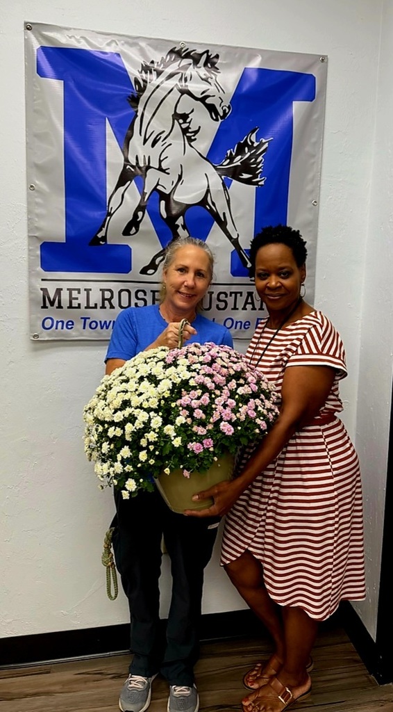 picture of 2 ladies holding a flower in front of a Mustang banner