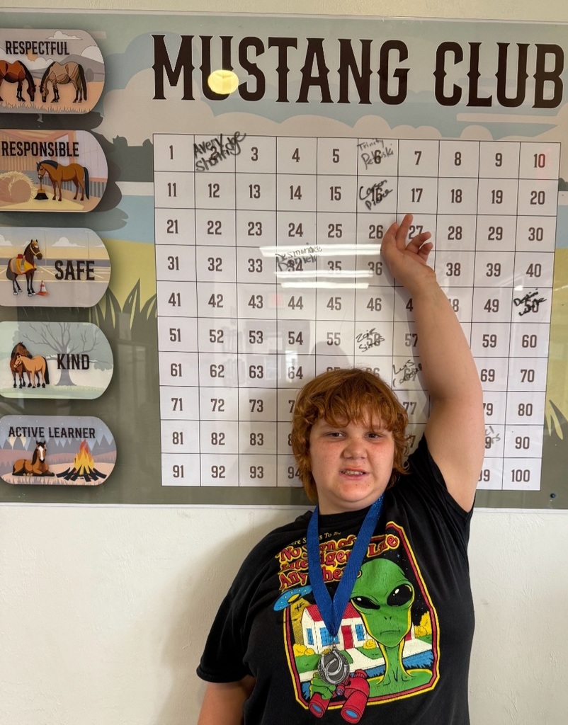 Picture of male student pointing at the Mustang Club board with his medal.