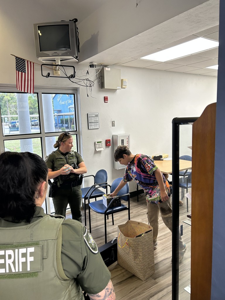 Picture of student opening a gift from 2 sheriff deputies.