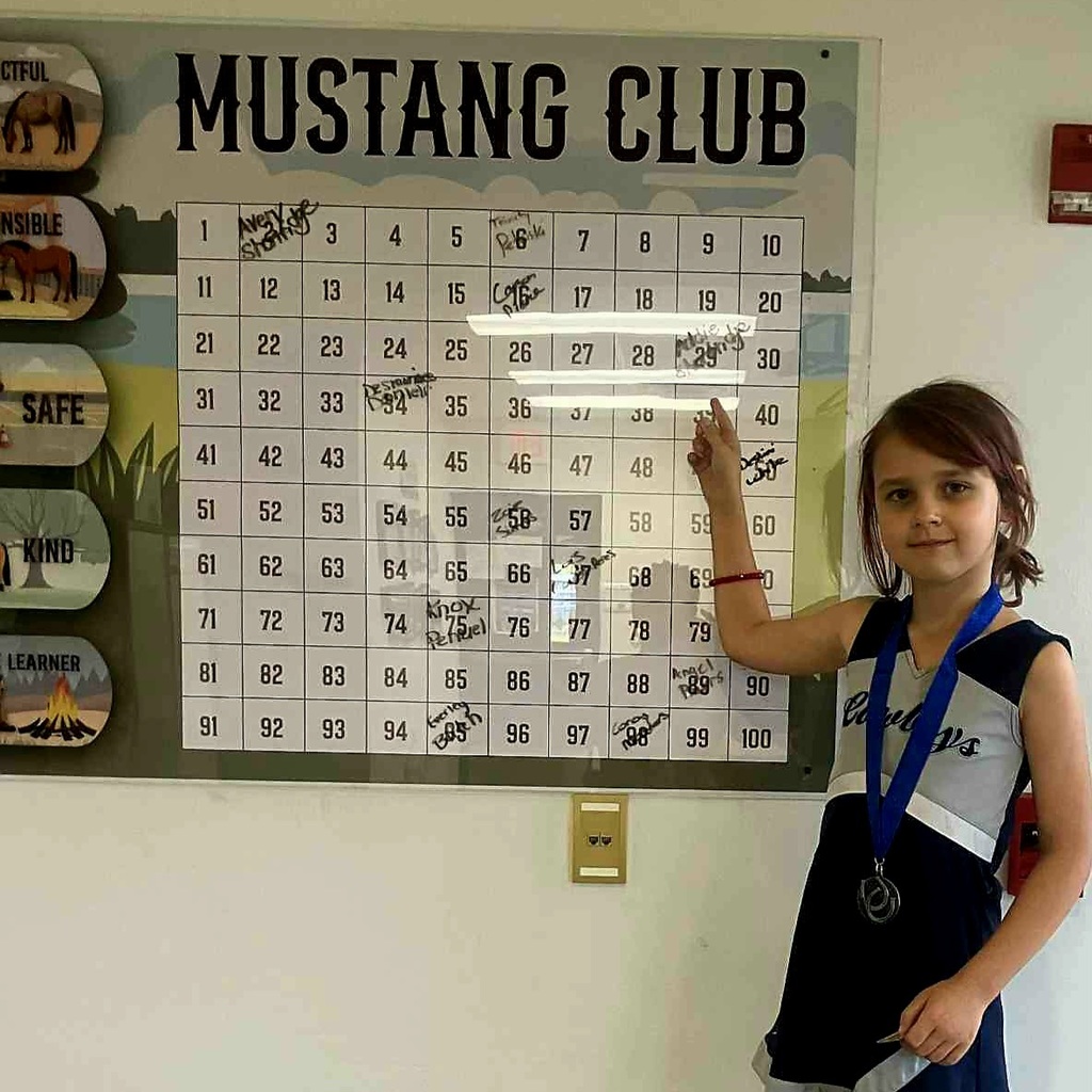 Picture of female student pointing at the Mustang Club board.