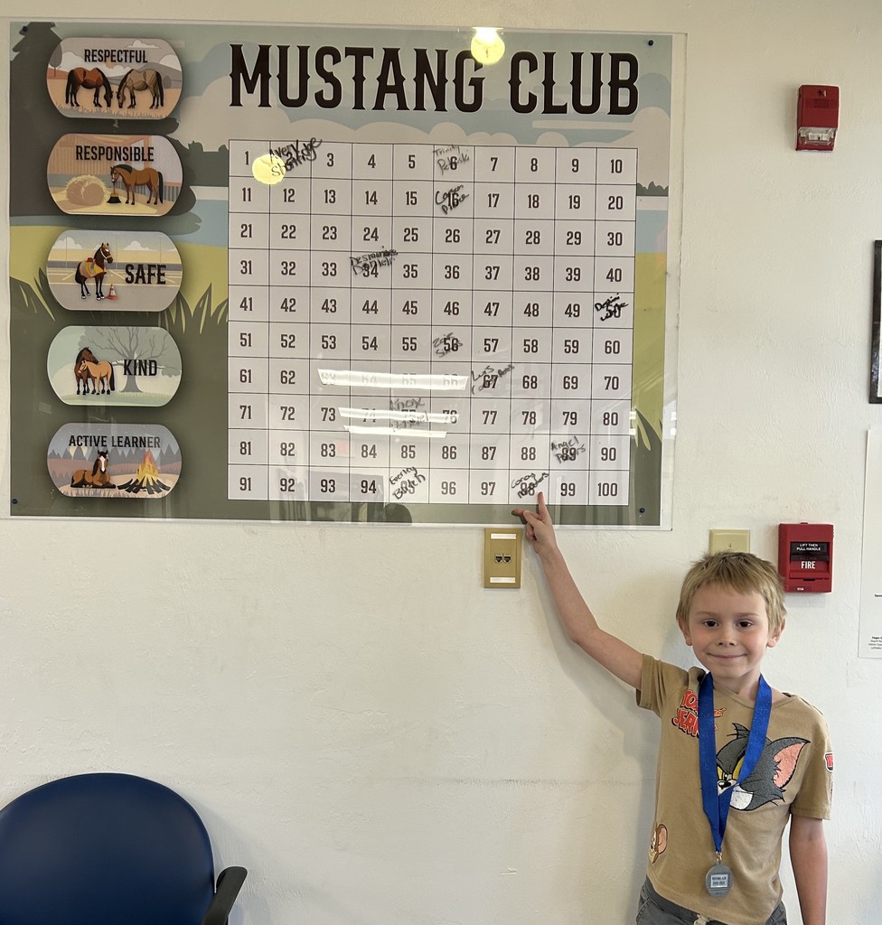 Picture of male student pointing at the Mustang Club board with his medal.