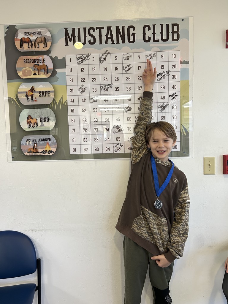 Picture of male student pointing at the Mustang Club board with his medal.