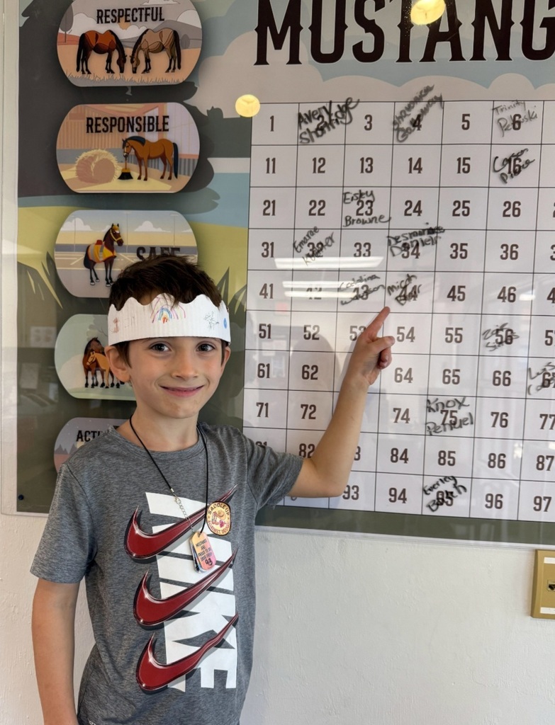 Picture of male student pointing at the Mustang Club board with his medal.