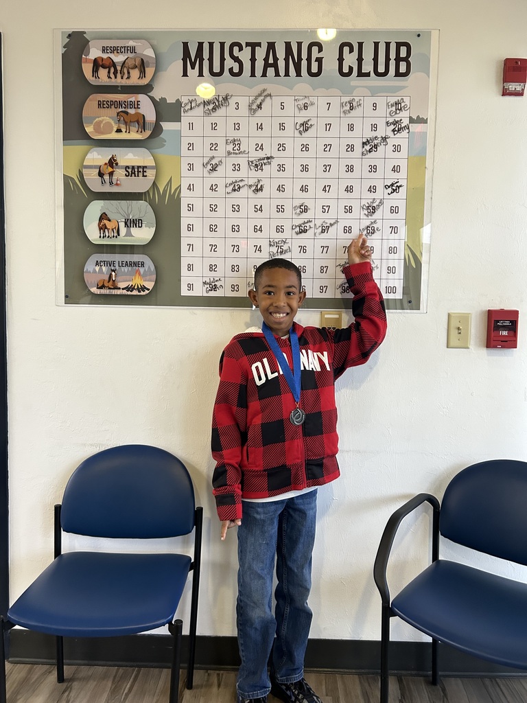 Picture of male student pointing at the Mustang Club board with his medal.