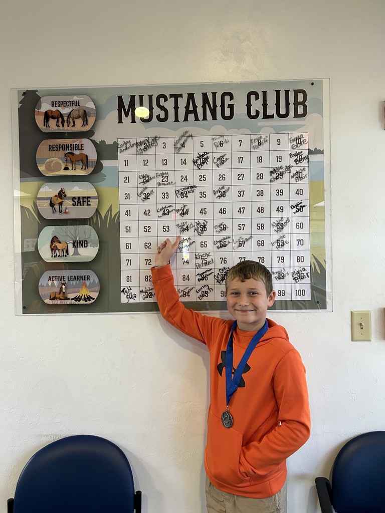 Picture of male student pointing at the Mustang Club board with his medal.