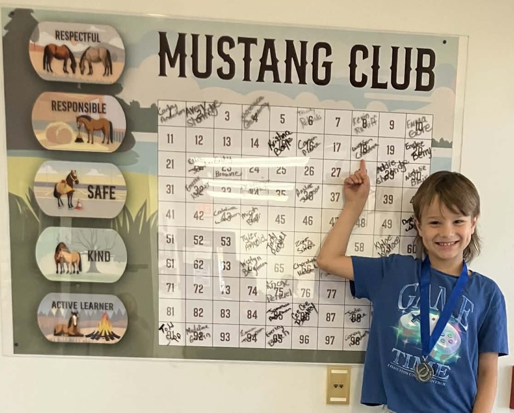Picture of male student pointing at the Mustang Club board with his medal.