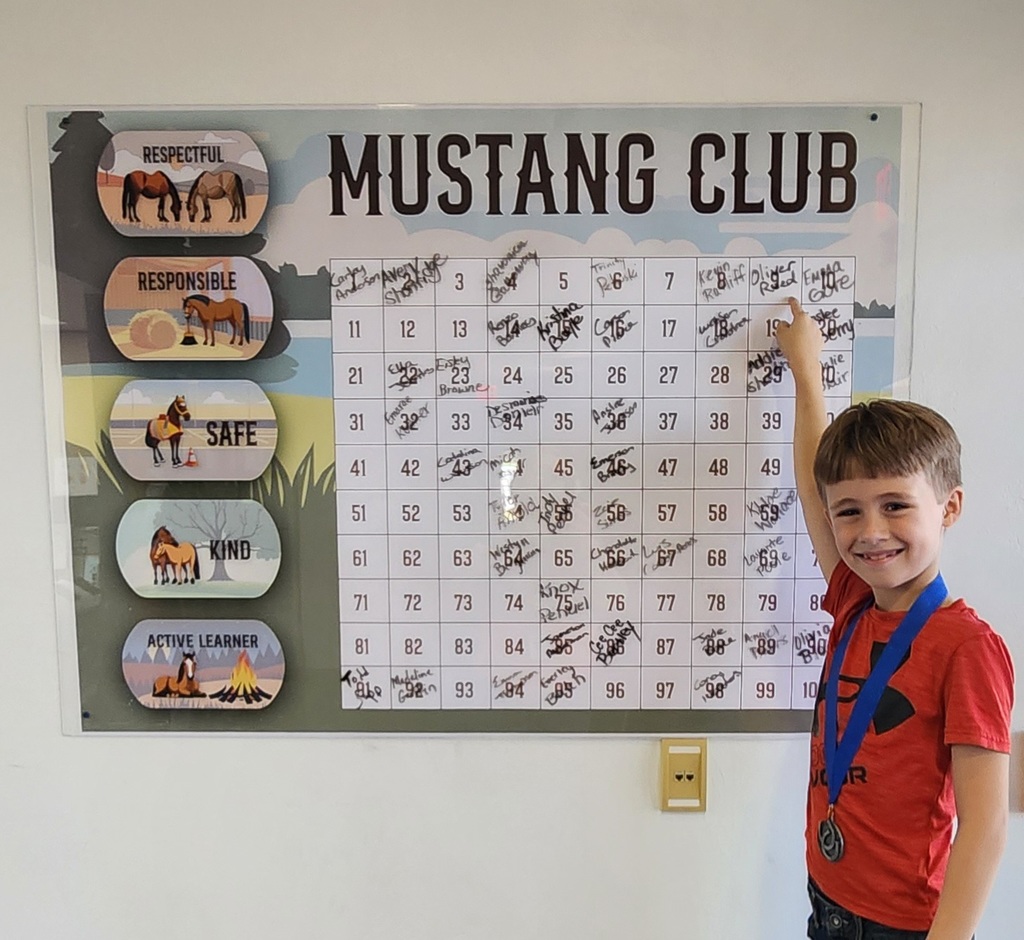 Picture of male student pointing at the Mustang Club board with his medal.