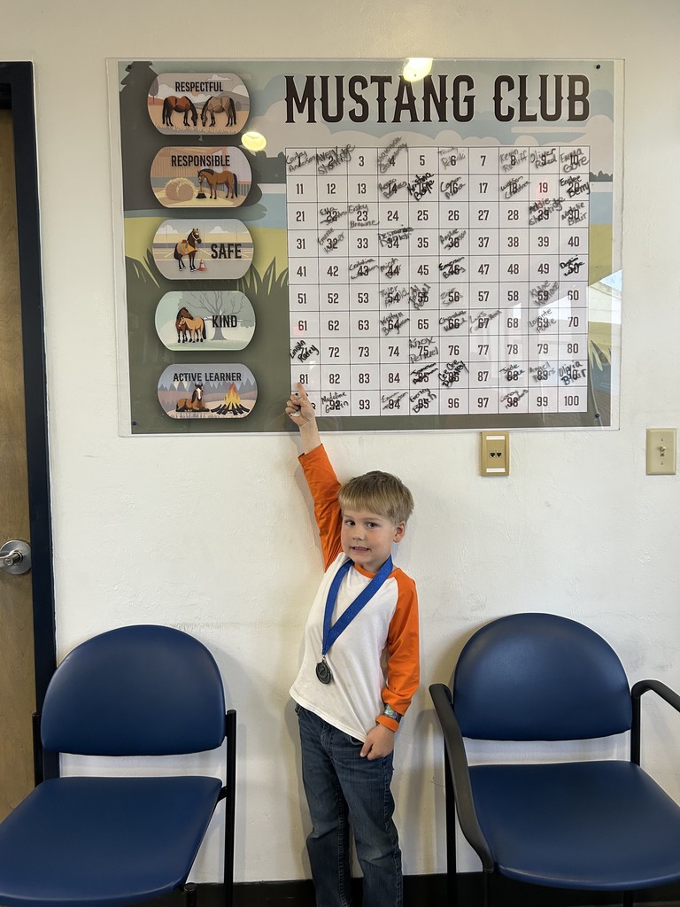 Picture of male student pointing at the Mustang Club board with his medal.