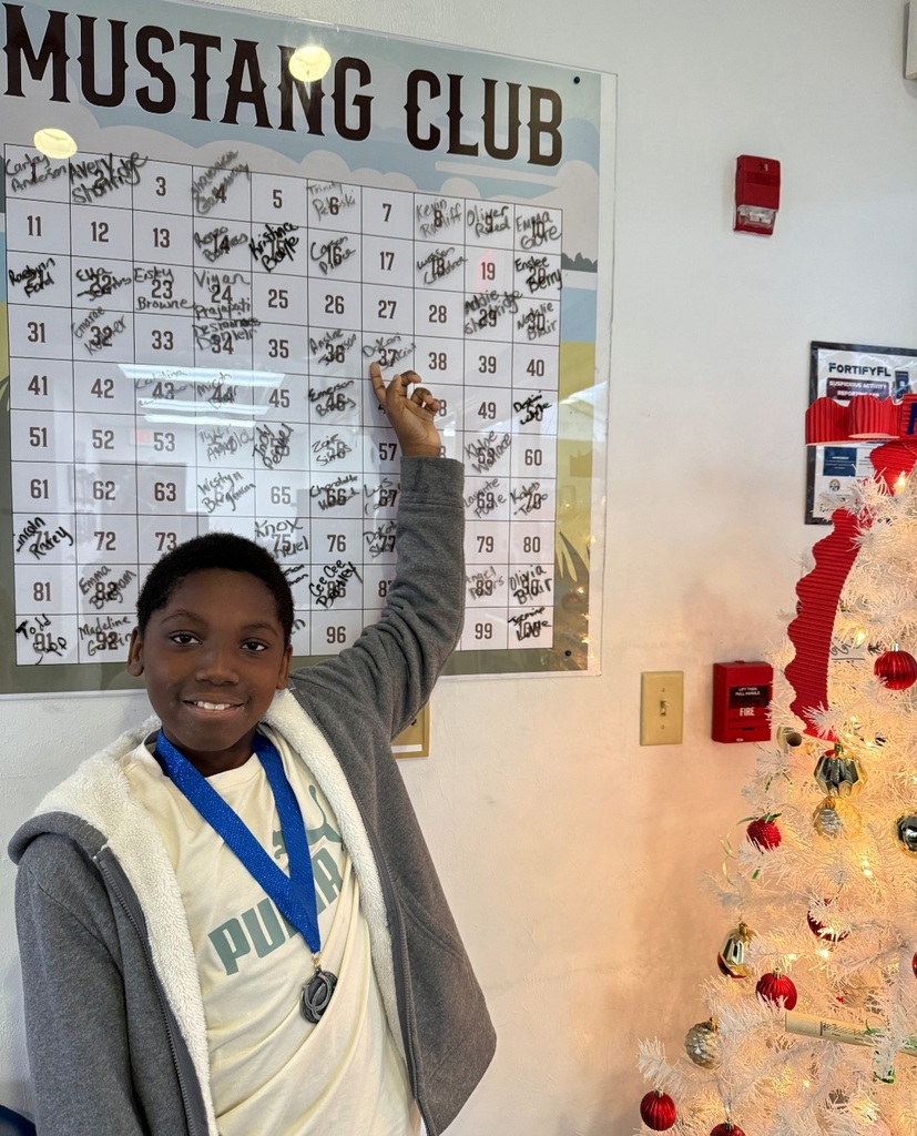 Picture of male student pointing at the Mustang Club board with his medal.