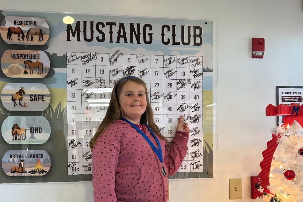 picture of female student pointing to Mustang Club board