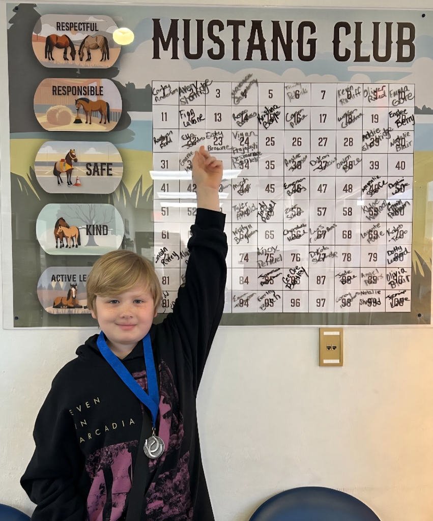 Picture of male student pointing at the Mustang Club board with his medal.