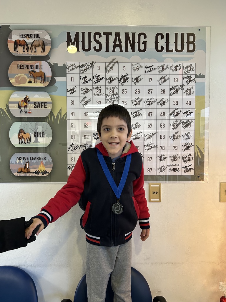 Picture of male student pointing at the Mustang Club board with his medal.