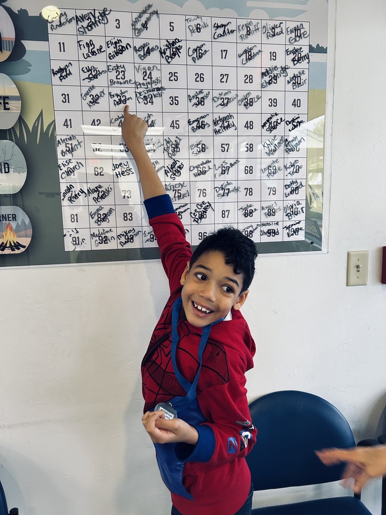 Picture of male student pointing at the Mustang Club board with his medal.