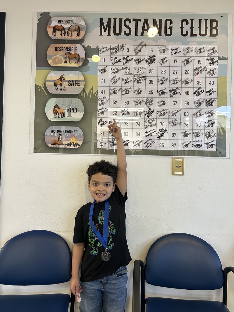 Picture of male student pointing at the Mustang Club board with his medal.