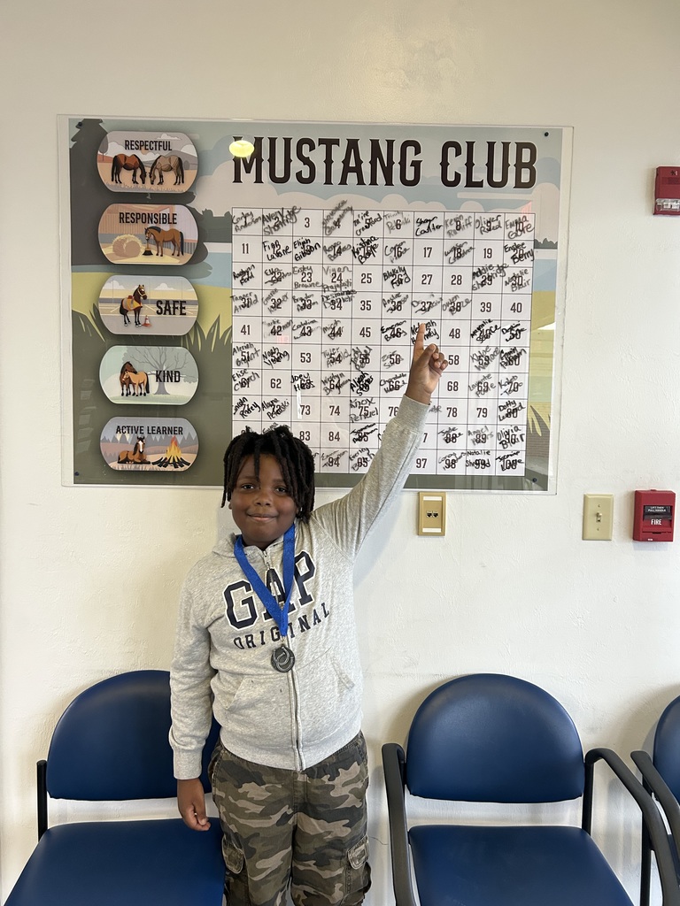 Picture of male student pointing at the Mustang Club board with his medal.