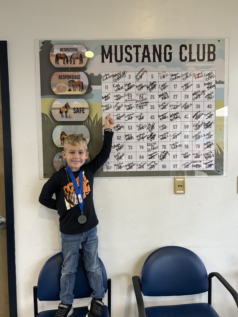 Picture of male student pointing at the Mustang Club board with his medal.