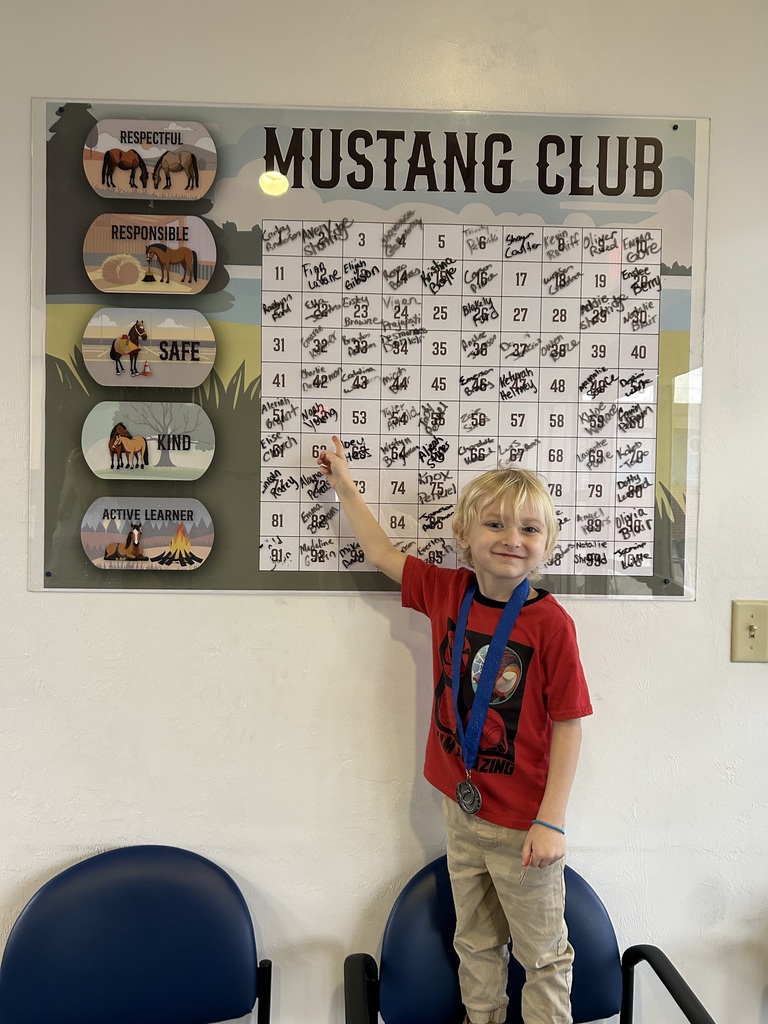 Picture of male student pointing at the Mustang Club board with his medal.
