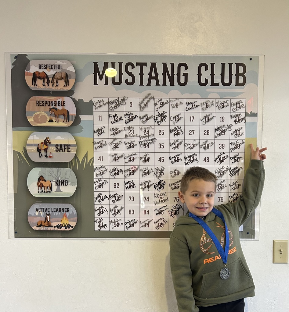 Picture of male student pointing at the Mustang Club board with his medal.