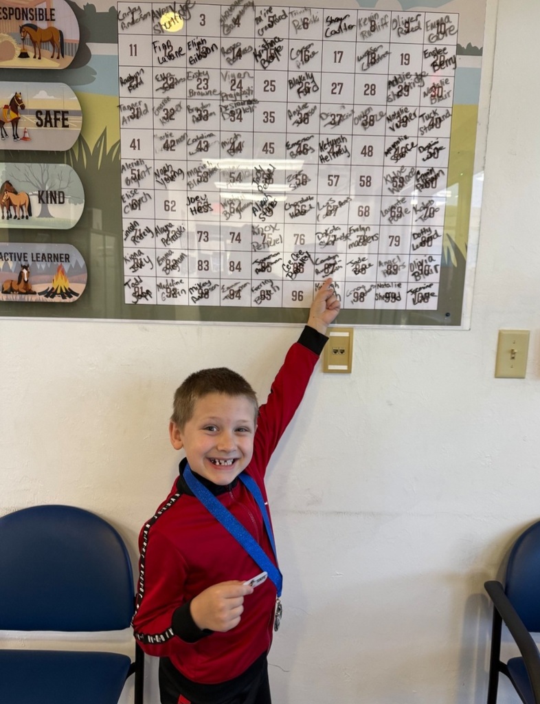 Picture of male student pointing at the Mustang Club board with his medal.