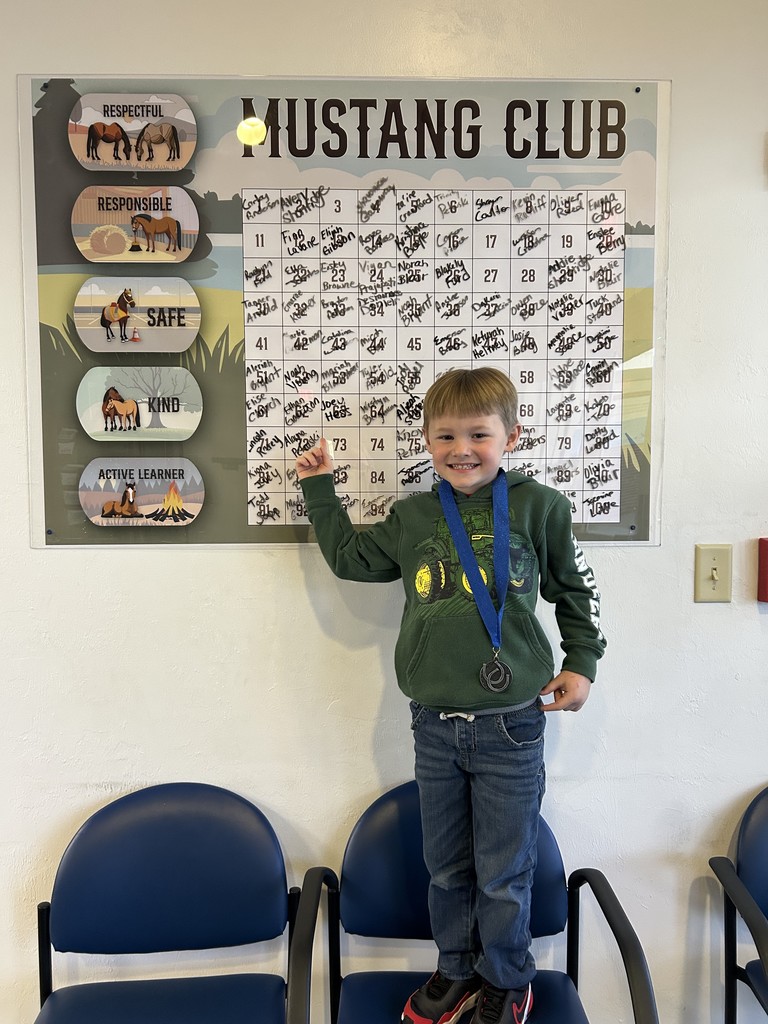 Picture of male student pointing at the Mustang Club board with his medal.