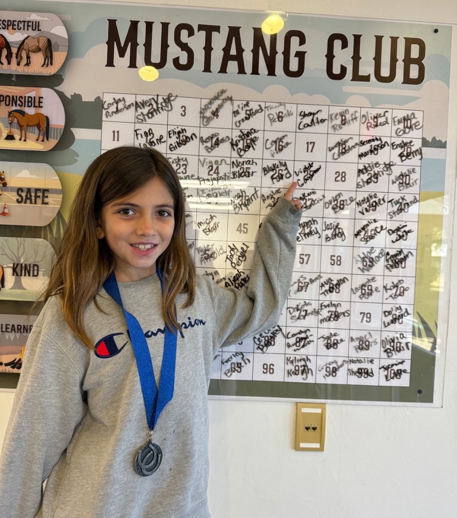 Picture of female student pointing at the Mustang Club board.