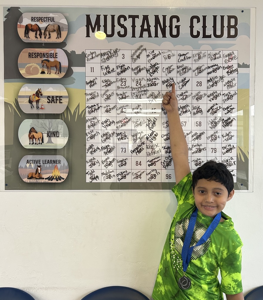 Picture of male student pointing at the Mustang Club board with his medal.