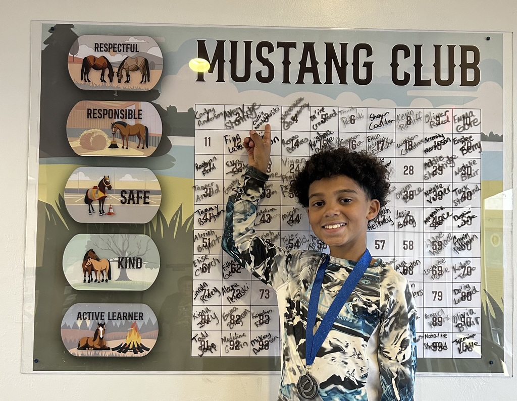 Picture of male student pointing at the Mustang Club board with his medal.
