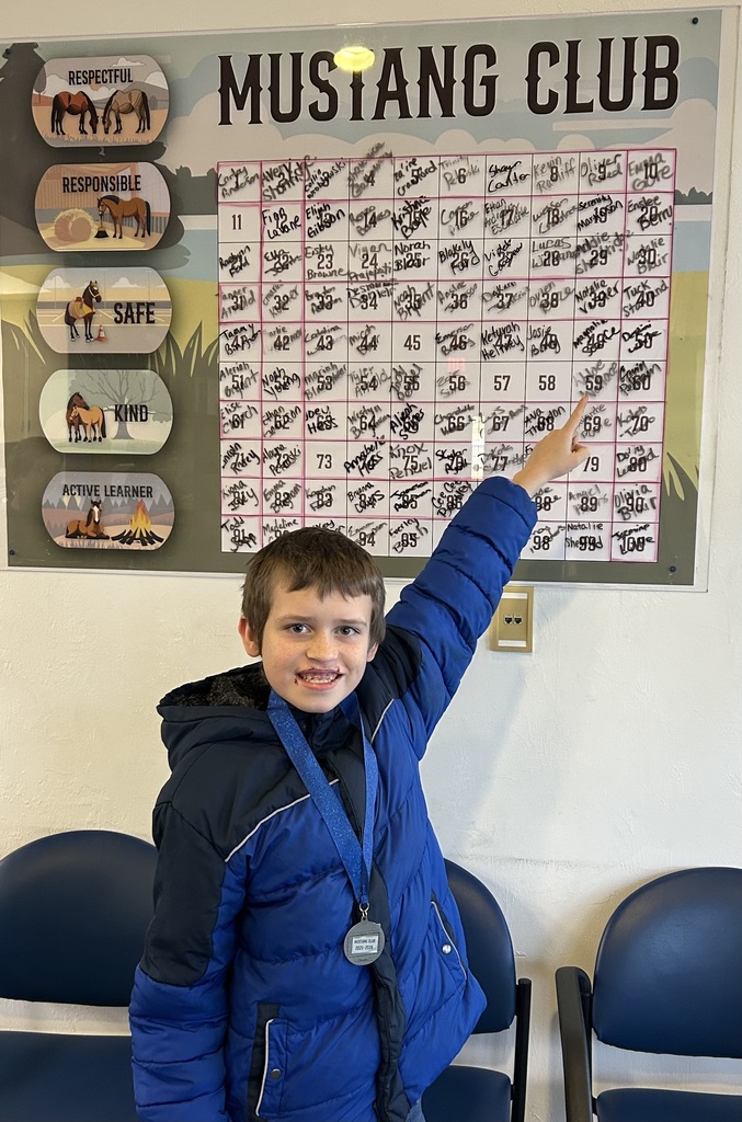 Picture of male student pointing at the Mustang Club board with his medal.