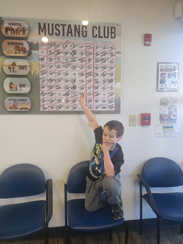 Picture of male student pointing at the Mustang Club board with his medal.