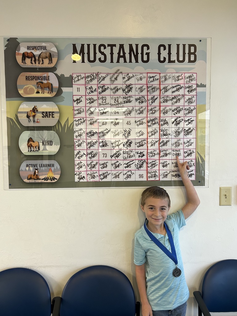 Picture of male student pointing at the Mustang Club board with his medal.